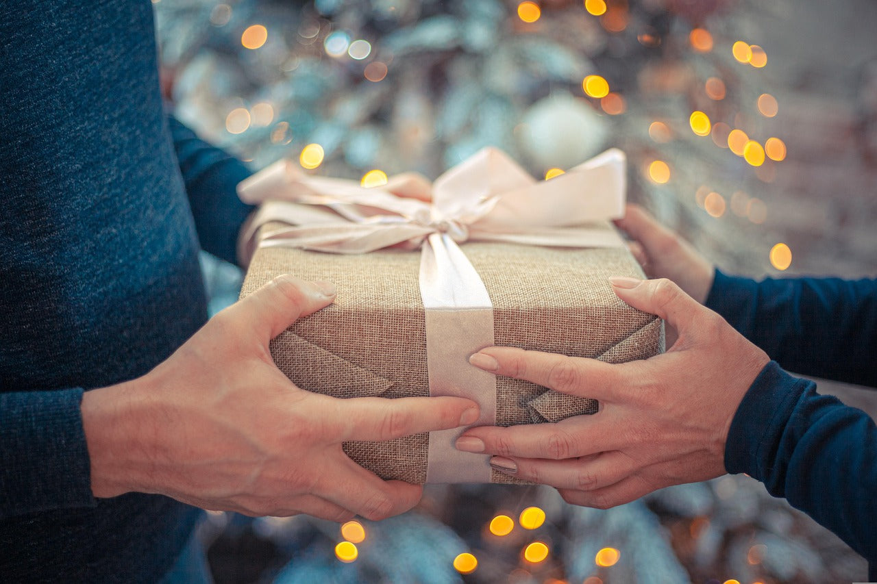 Two hands holding a gift box with a ribbon against a blurred festive background